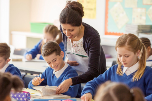 Female Supply Staff Member helping pupil with a text book